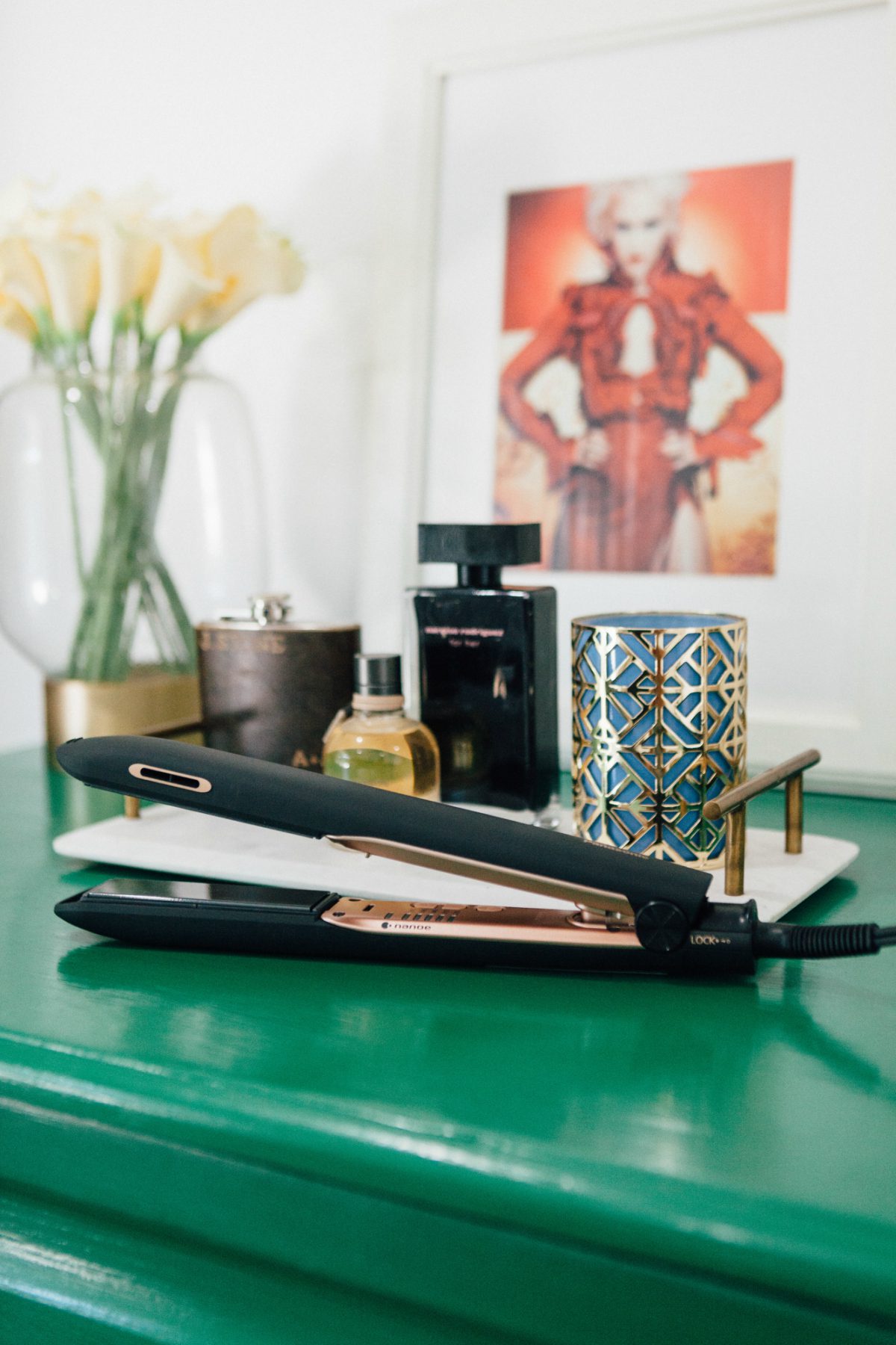 panasonic styling flat iron, perfumes, flowers, and a frame on top of a green surface